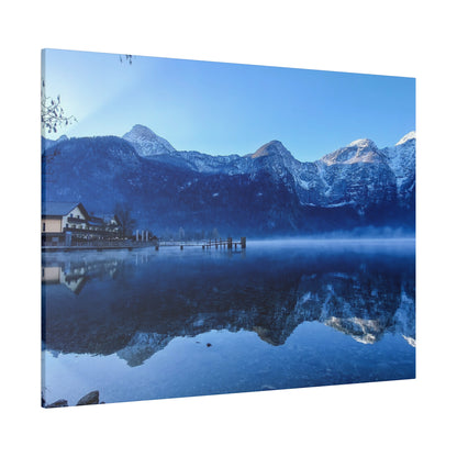 Blue alpine lake at dawn reflecting snow-capped mountains and a small lodge on the left.