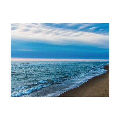 A sandy beach with blue ocean waves rolling onto the shore under a cloudy blue sky.