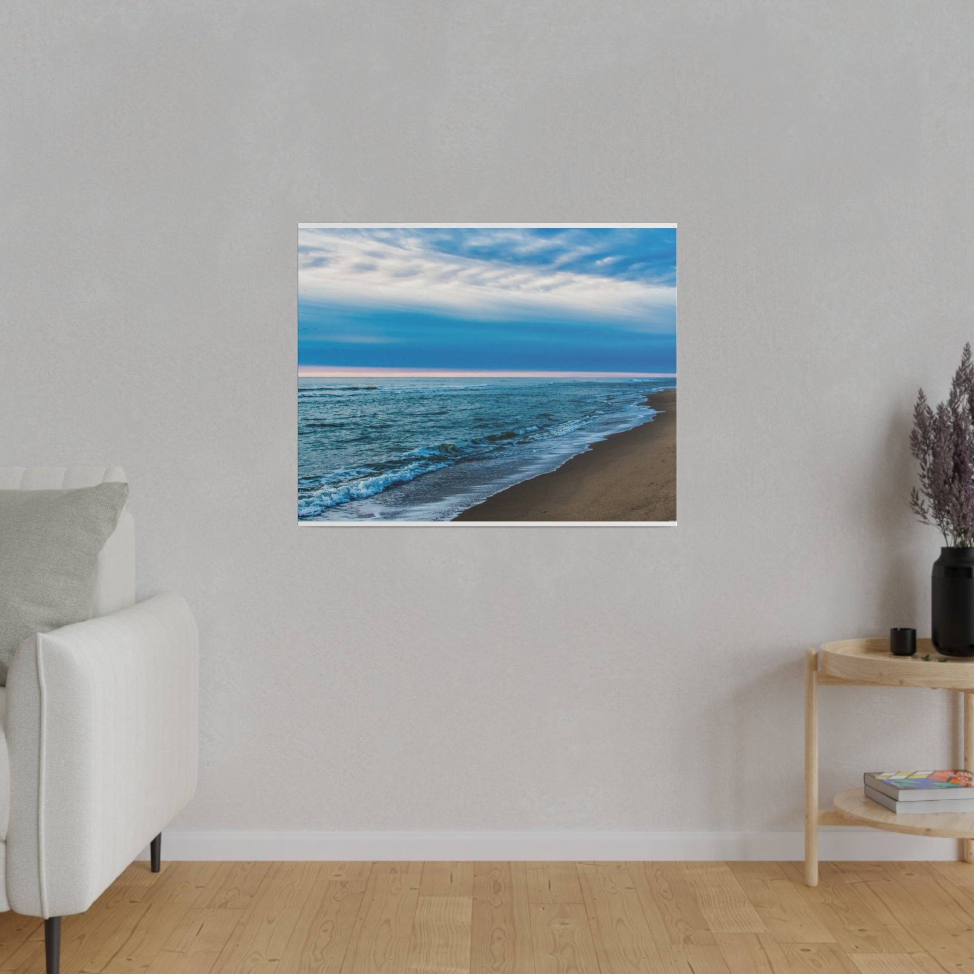 A framed beach photograph with blue ocean and brown sand hangs on a light gray living room wall above a light-colored sofa.