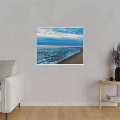 A framed beach photograph with blue ocean and brown sand hangs on a light gray living room wall above a light-colored sofa.