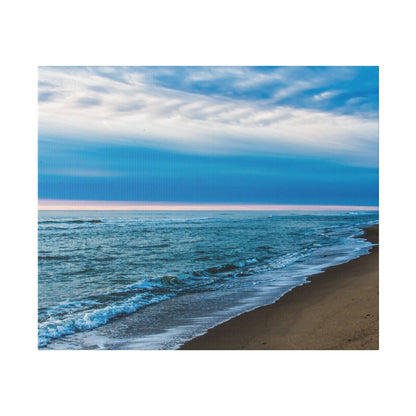A sandy beach with blue waves washing ashore under a bright blue sky and pink horizon line.