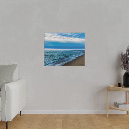 Square wall art print of a blue ocean beach with waves on a beige sandy shore, mounted on a light gray wall.