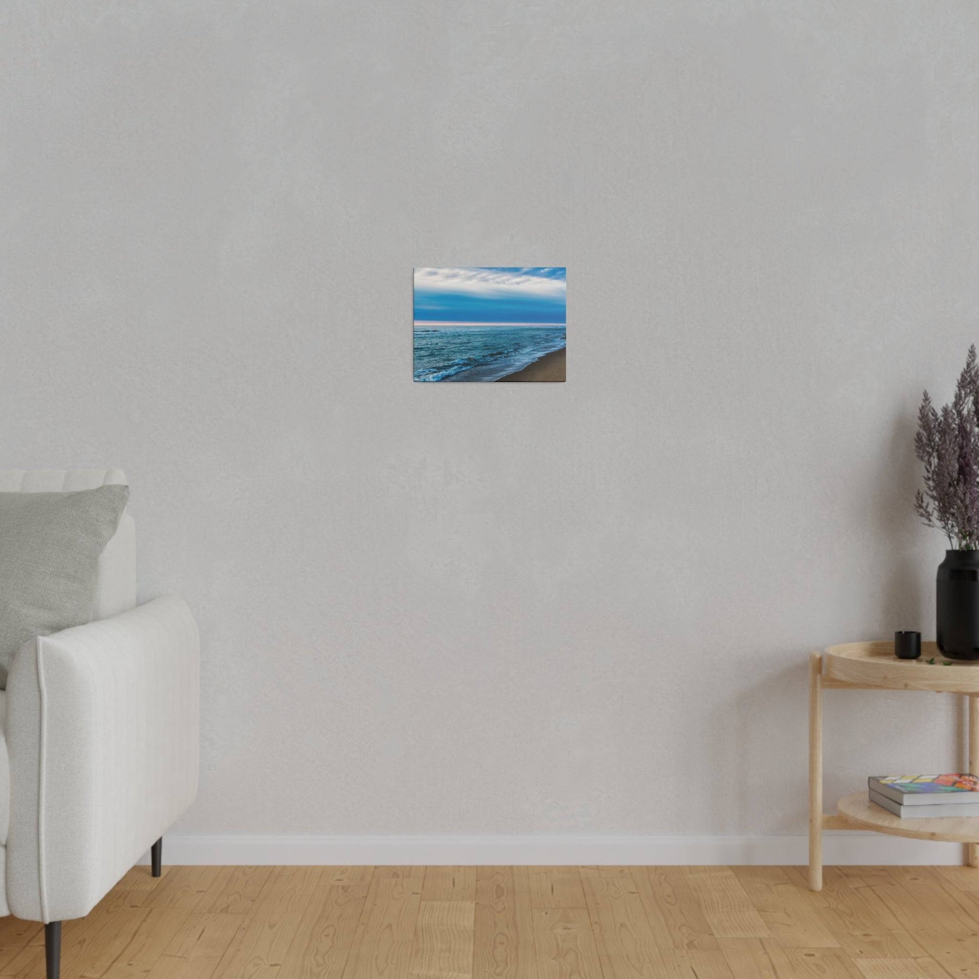 Small square painting of a blue ocean and sandy beach, hung on a light gray wall in a minimalist living room.