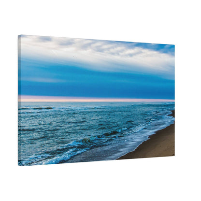 Canvas wall art depicting a blue ocean shoreline with waves washing onto a sandy beach under a cloudy sky.