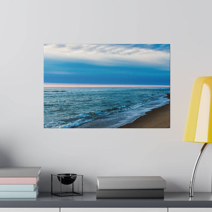 Canvas wall art showing a blue ocean and sandy beach under a pale sky, mounted above a desk with books.