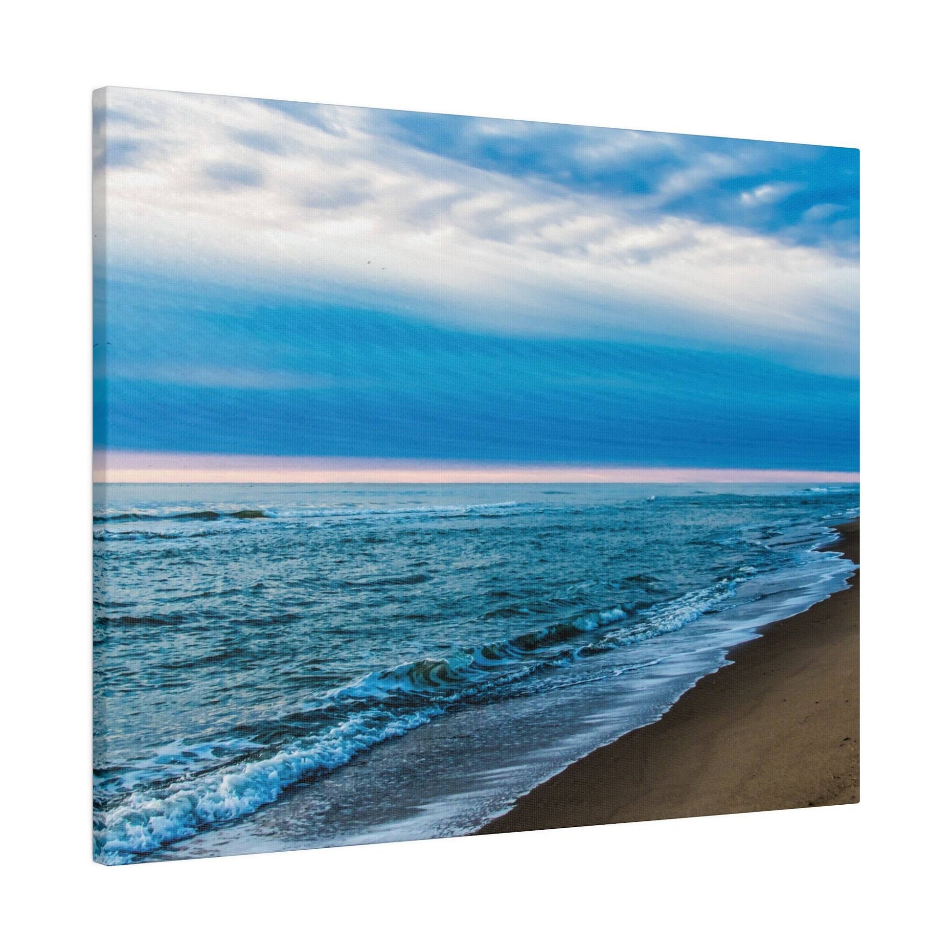 Beach scene with brown sand, blue ocean waves washing ashore, and a blue sky with white clouds.