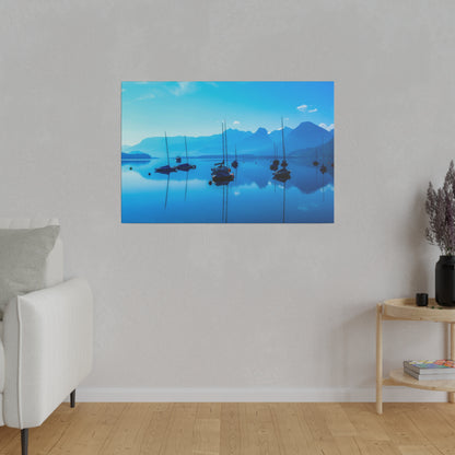 Photograph of a blue lake with anchored sailboats and distant mountains, reflections visible on the calm water.