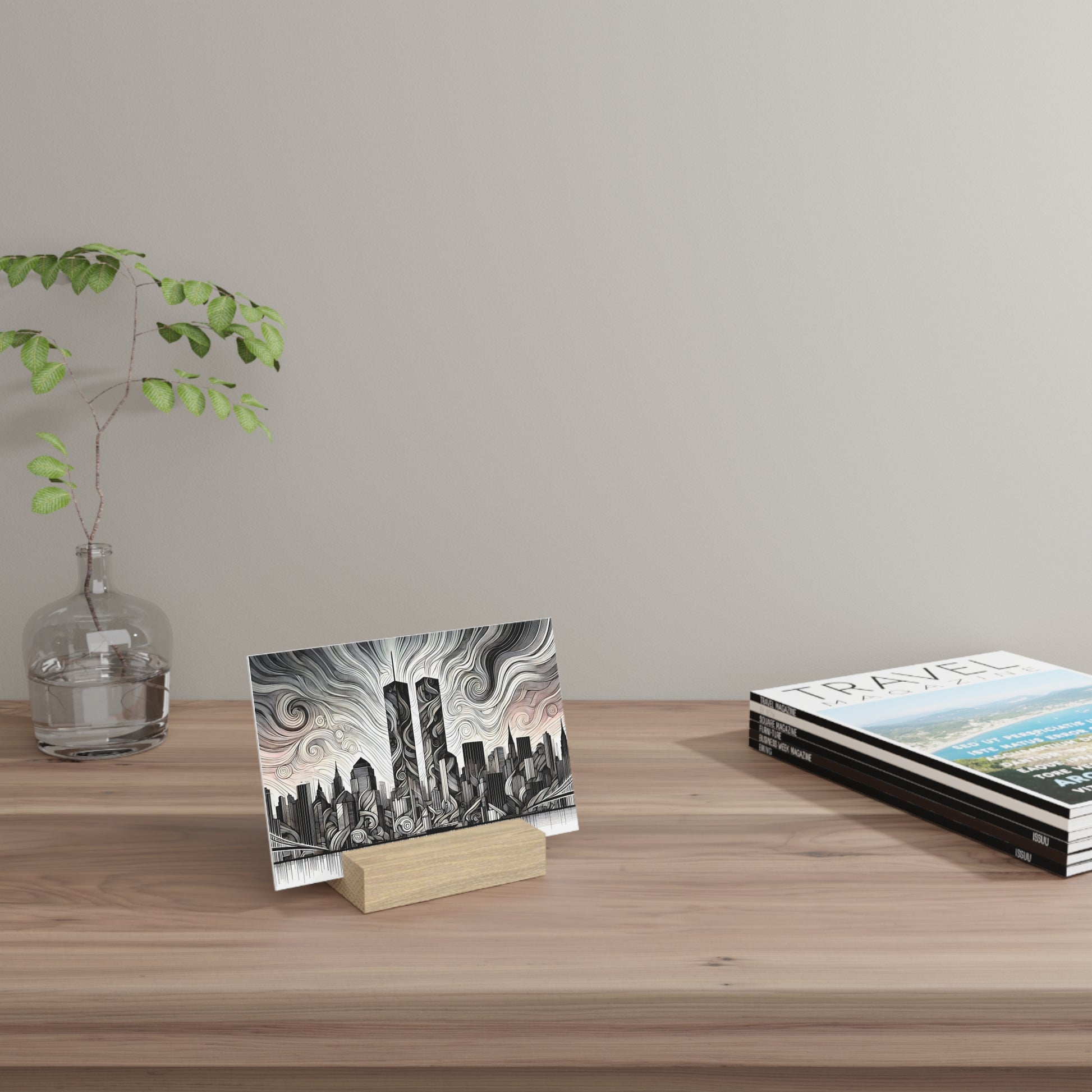 A wooden desk with a glass vase holding a leafy branch on the left, a black-and-white cityscape art print on a wooden block in the center,