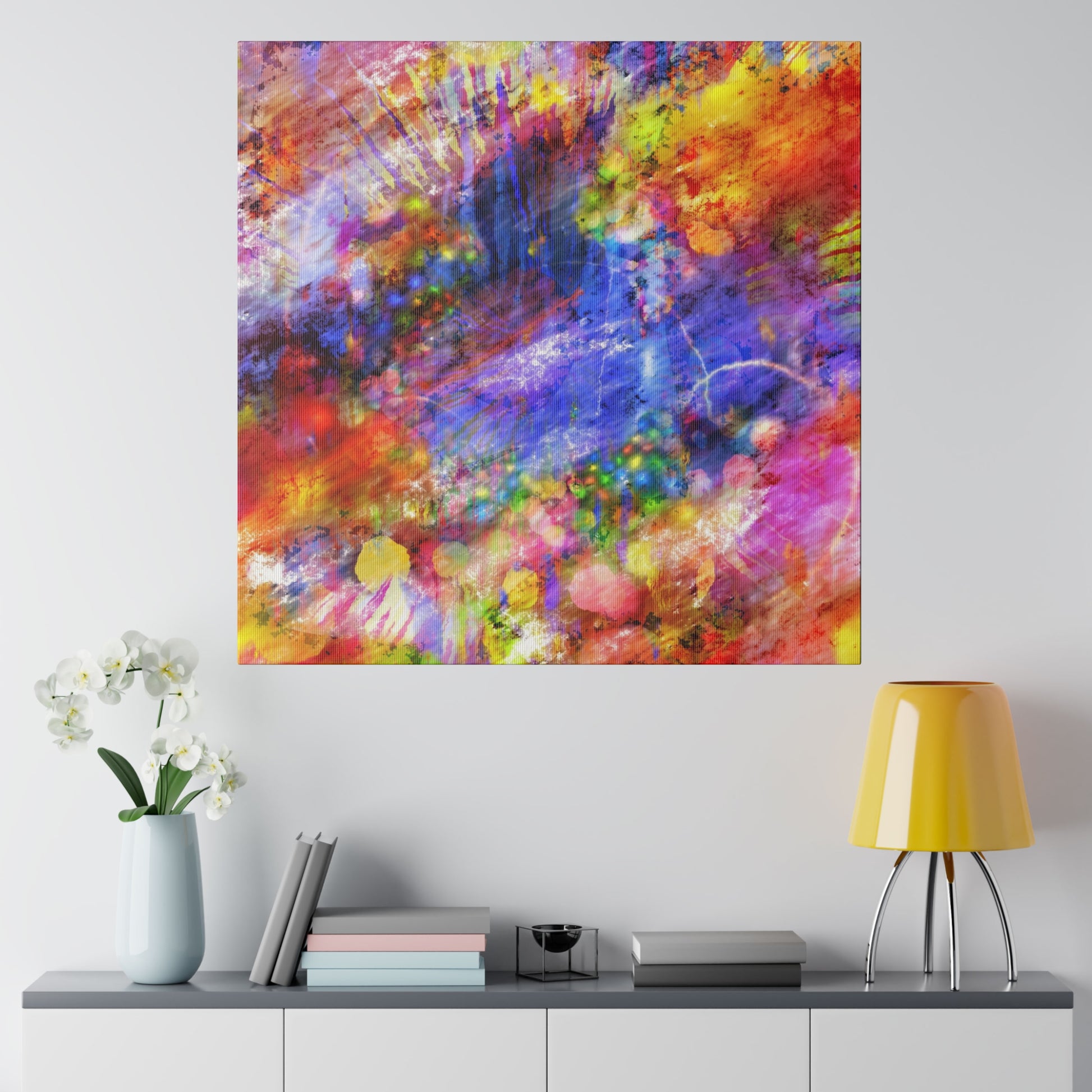 Abstract colorful acrylic painting with red, blue, yellow and purple splashes hanging on a light gray wall above a sideboard.