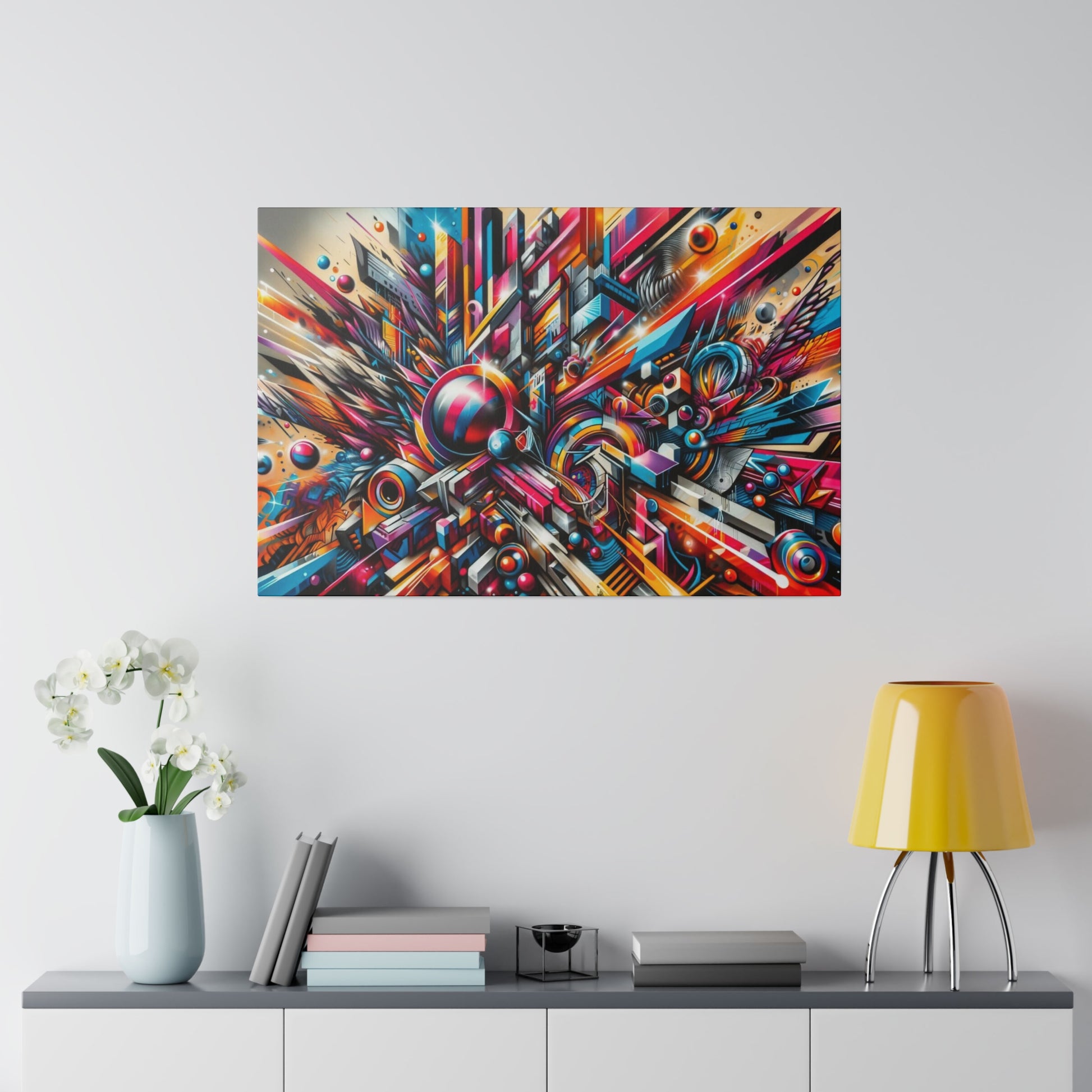 Colorful abstract geometric painting on the wall above a gray console table with a white orchid vase, books, and a yellow lamp.