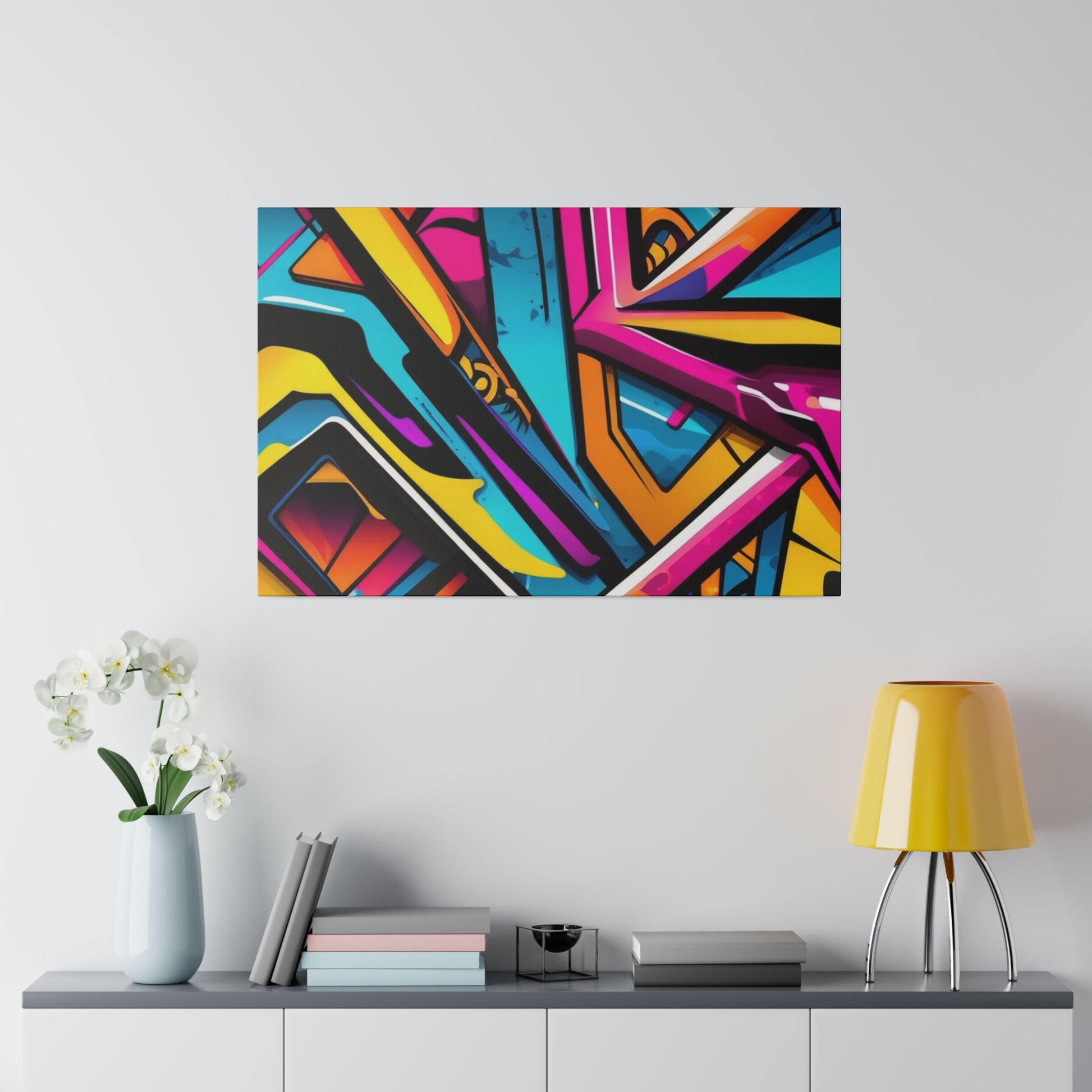 Colorful abstract graffiti painting with geometric shapes hanging on a white wall above a gray console table.