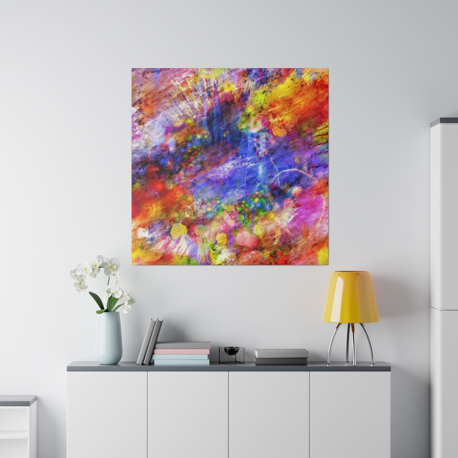 Abstract multicolor painting hung above a white sideboard with a yellow lamp and a vase of white orchids.