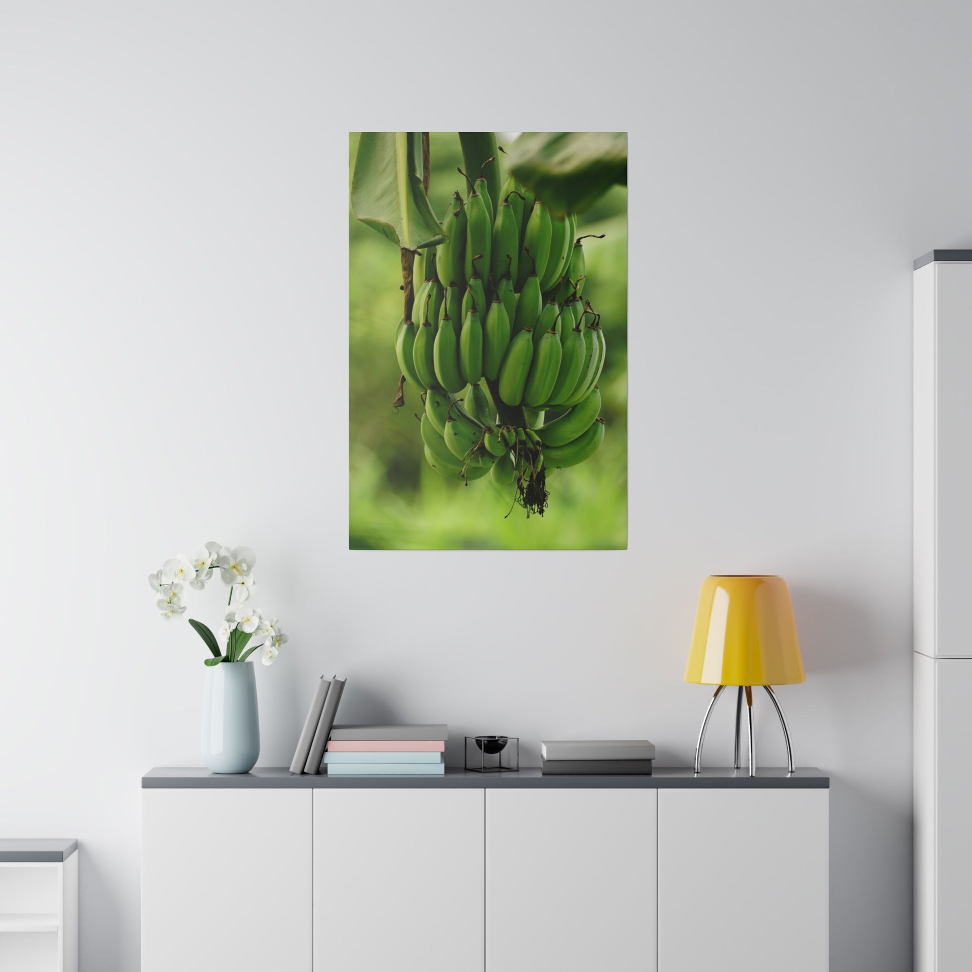 Tall wall art showing a cluster of ripe green bananas on a banana plant, hung above a white cabinet in a modern living room.