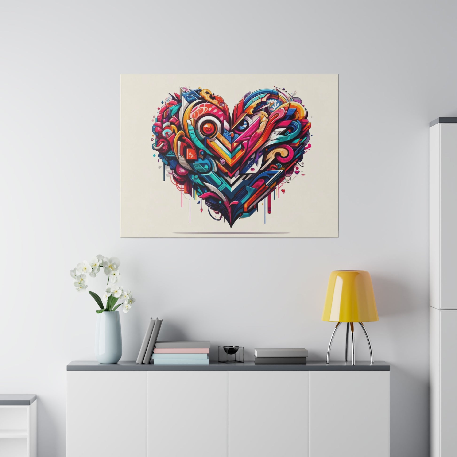 Colorful abstract heart graffiti art on a light wall above a white cabinet with a yellow lamp and white orchid vase.