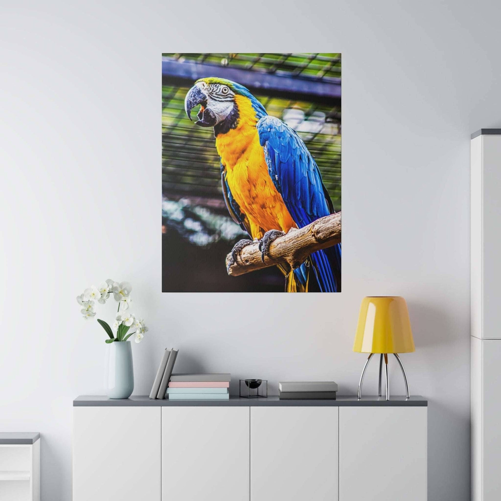 Large canvas print of a blue-and-yellow macaw parrot perched on a branch indoors above a white cabinet.
