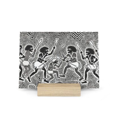 Black and white tribal-style print of dancing figures with spears, mounted on a light wooden display block.