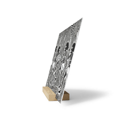 Black-and-white patterned poster leaning on a small light wooden block stand on a white background.