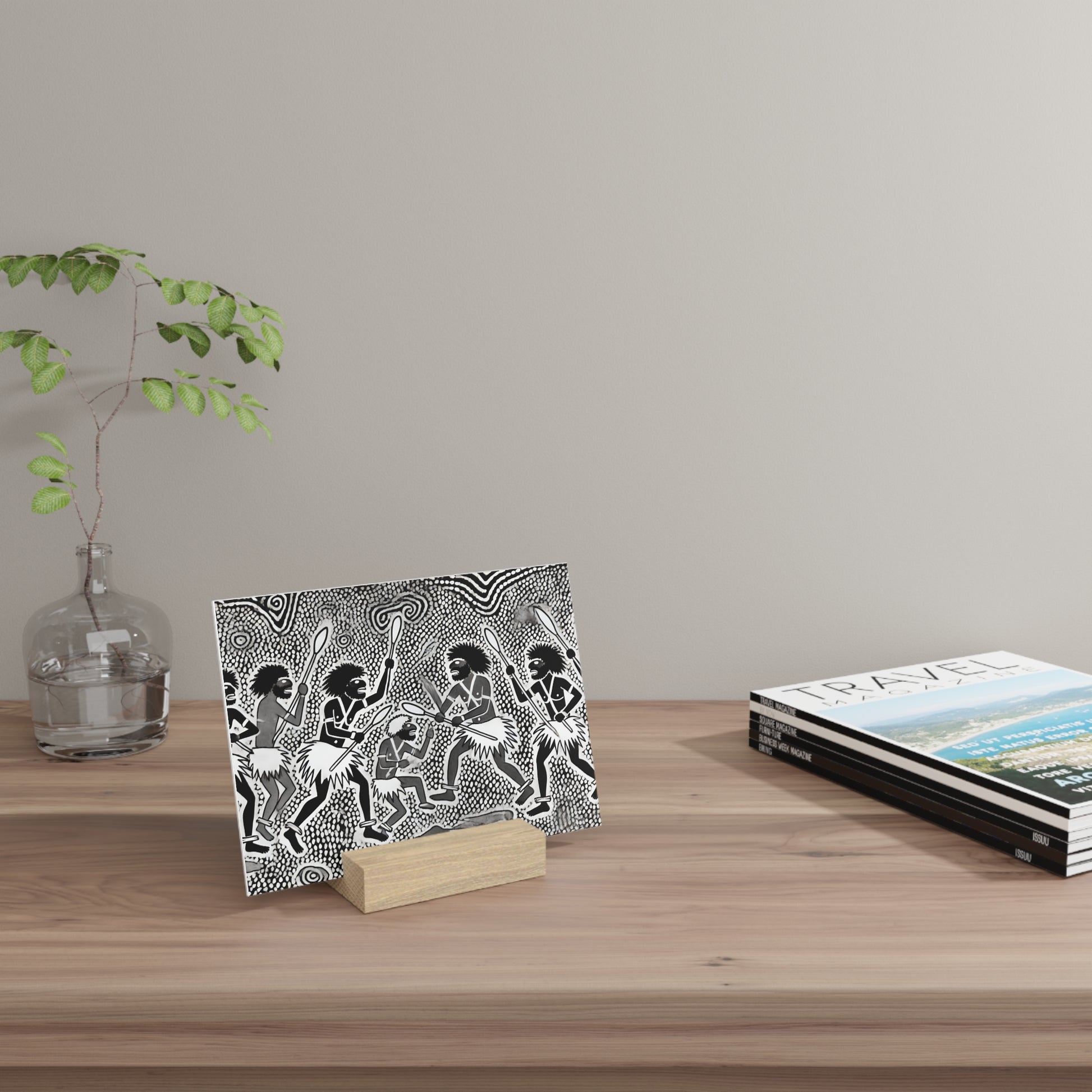 A black-and-white patterned card on a small wooden stand sits on a light wooden table, with a glass vase and magazines nearby.