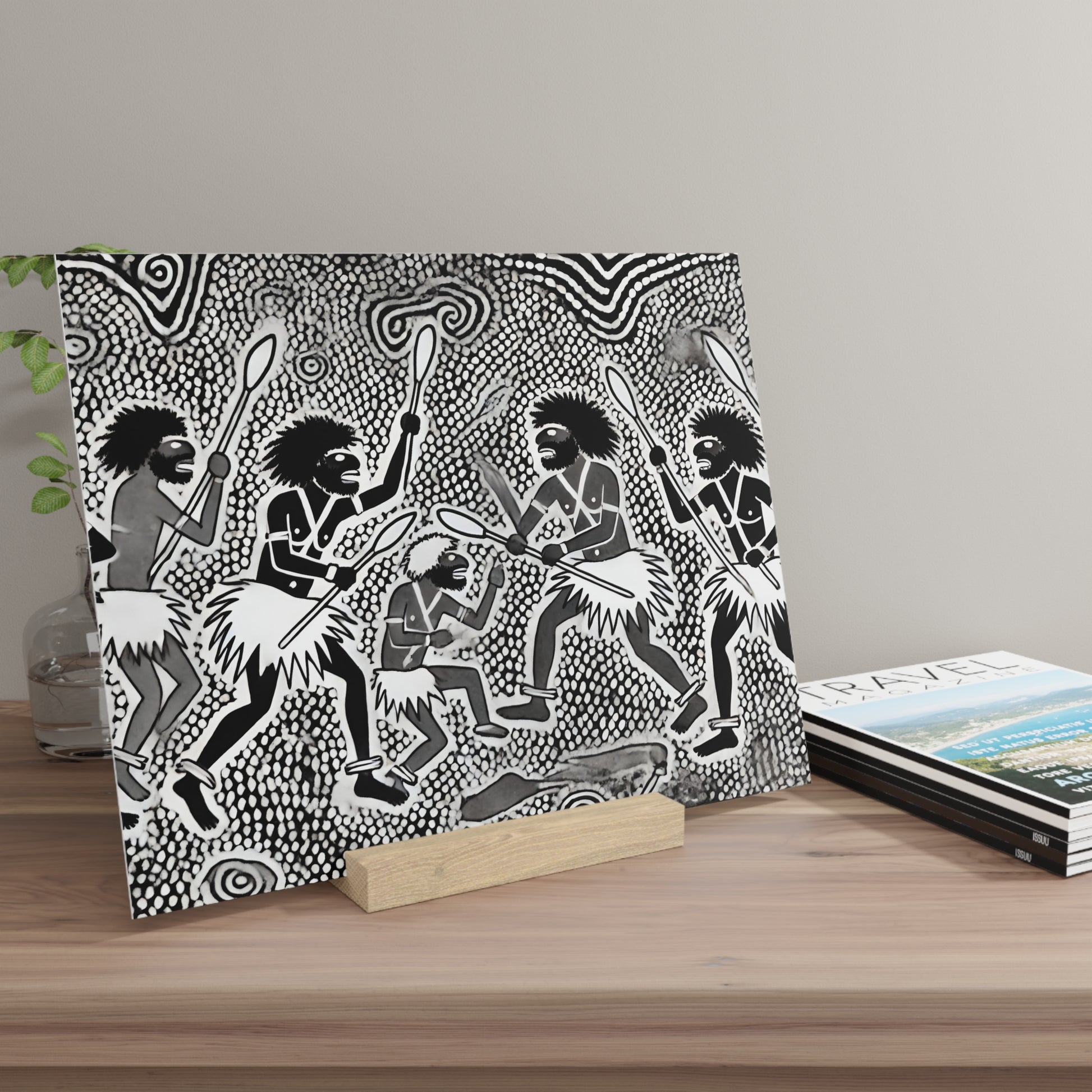 Square black-and-white tribal painting showing dancers with spears and grass skirts against a dotted patterned background, on a wooden