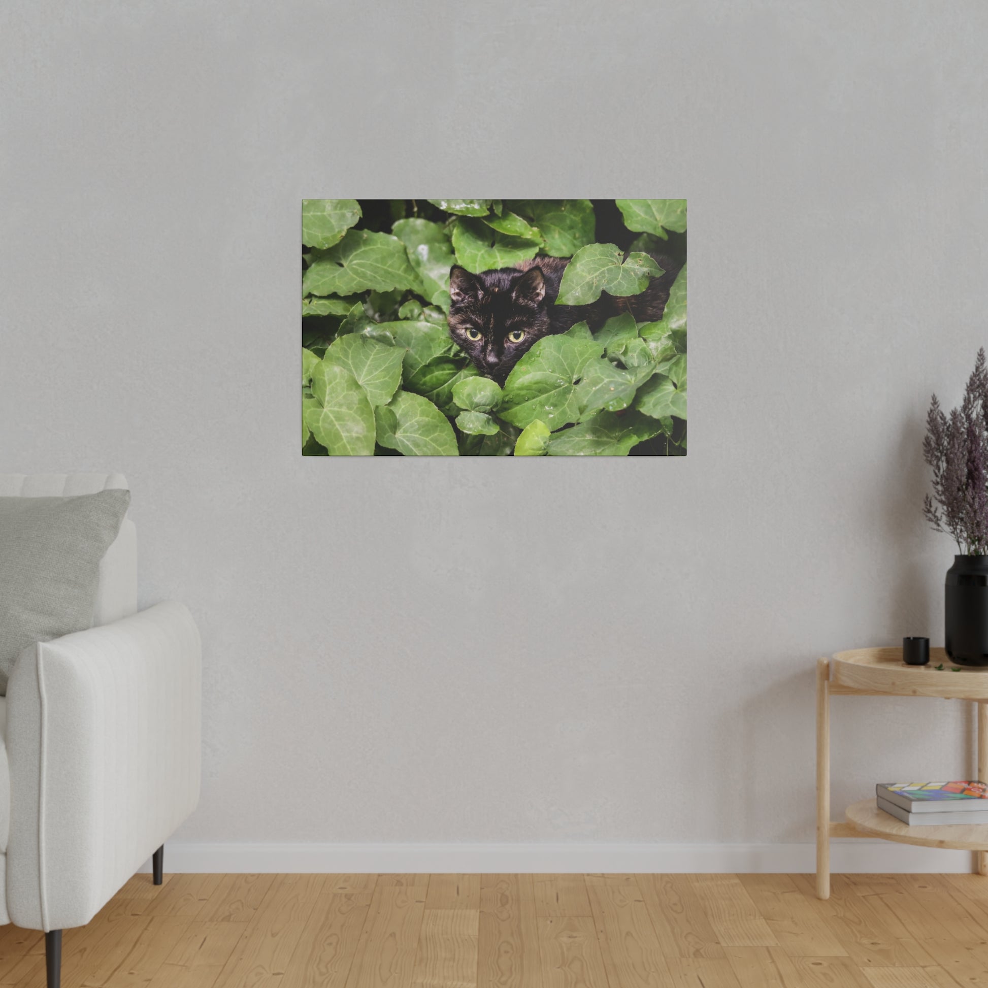Framed print of a black cat peeking through dense green ivy leaves on a light gray wall.