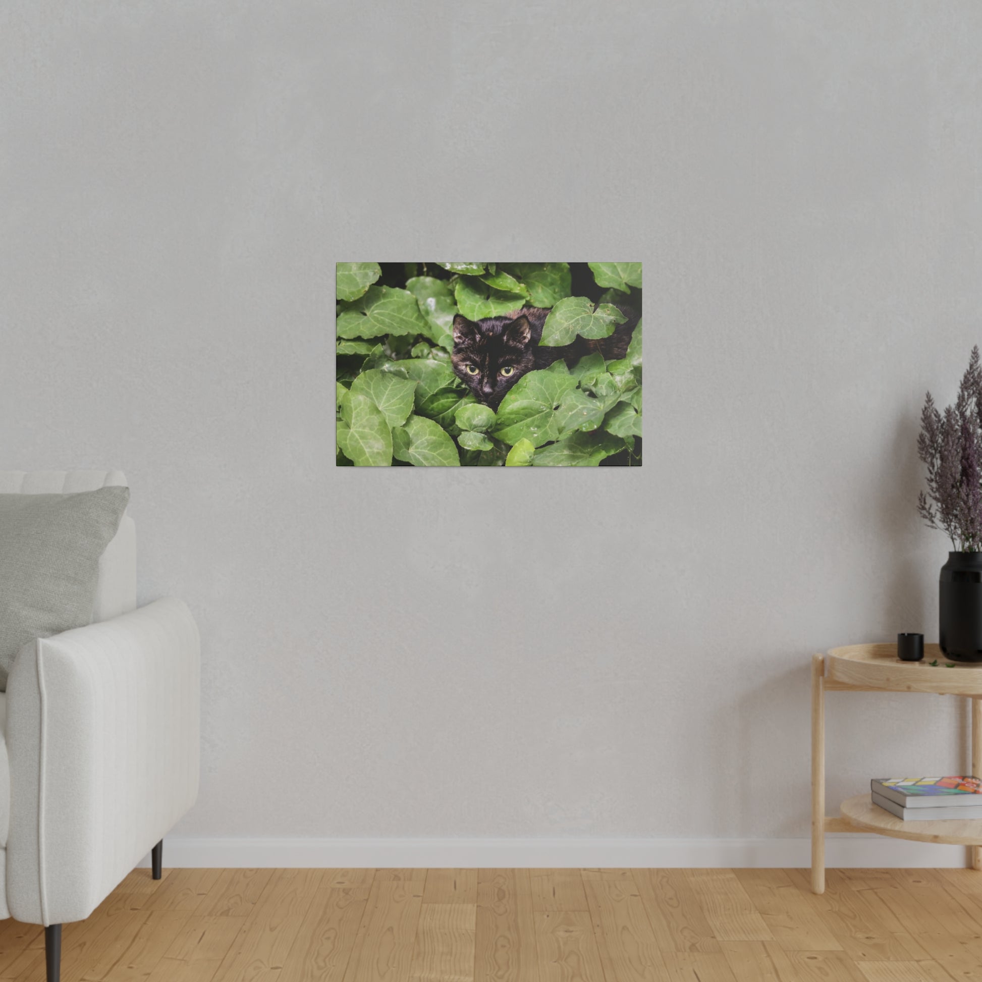 Small rectangular wall art showing a black cat peeking through dense green ivy leaves.