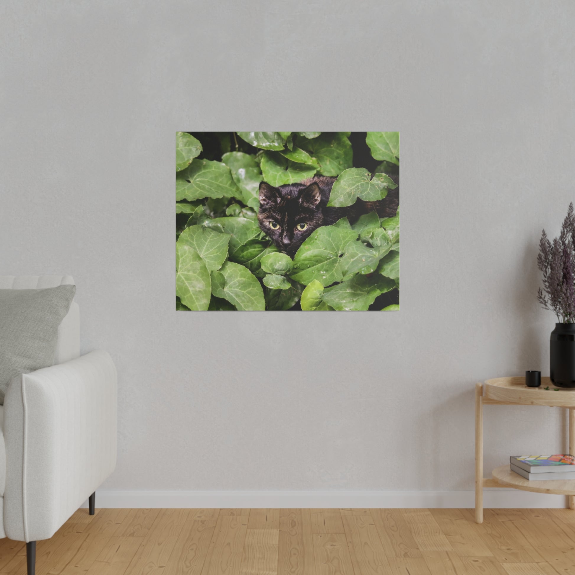 Square wall art showing a black cat peeking through dense green ivy leaves.