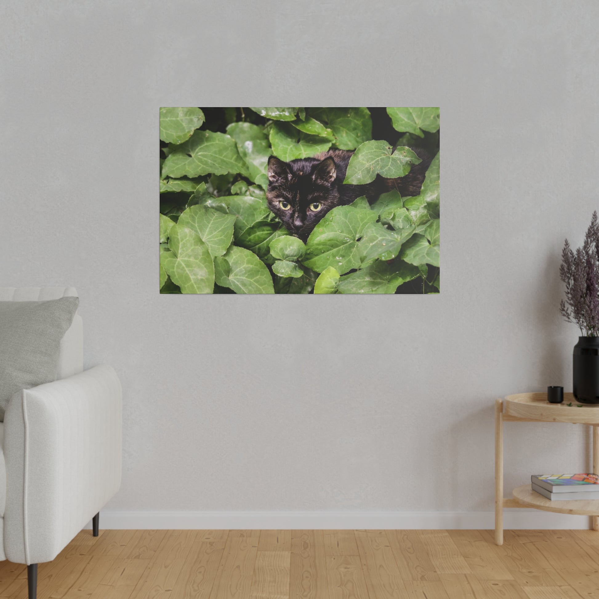 Framed wall art of a black cat peering through dense green ivy leaves.