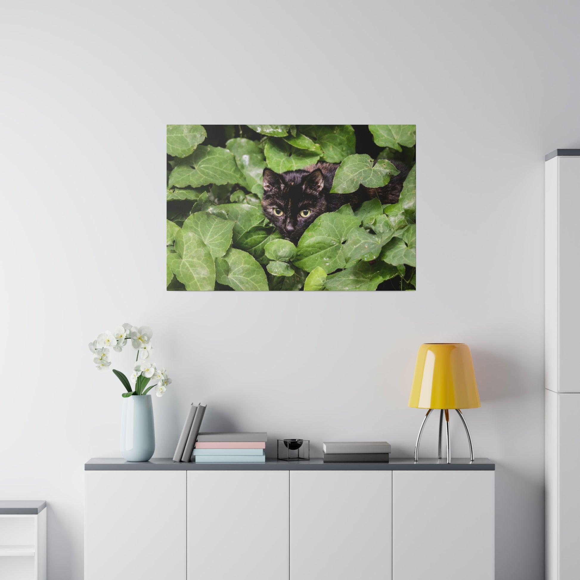 Close-up image of a black cat peeking from dense green ivy leaves.