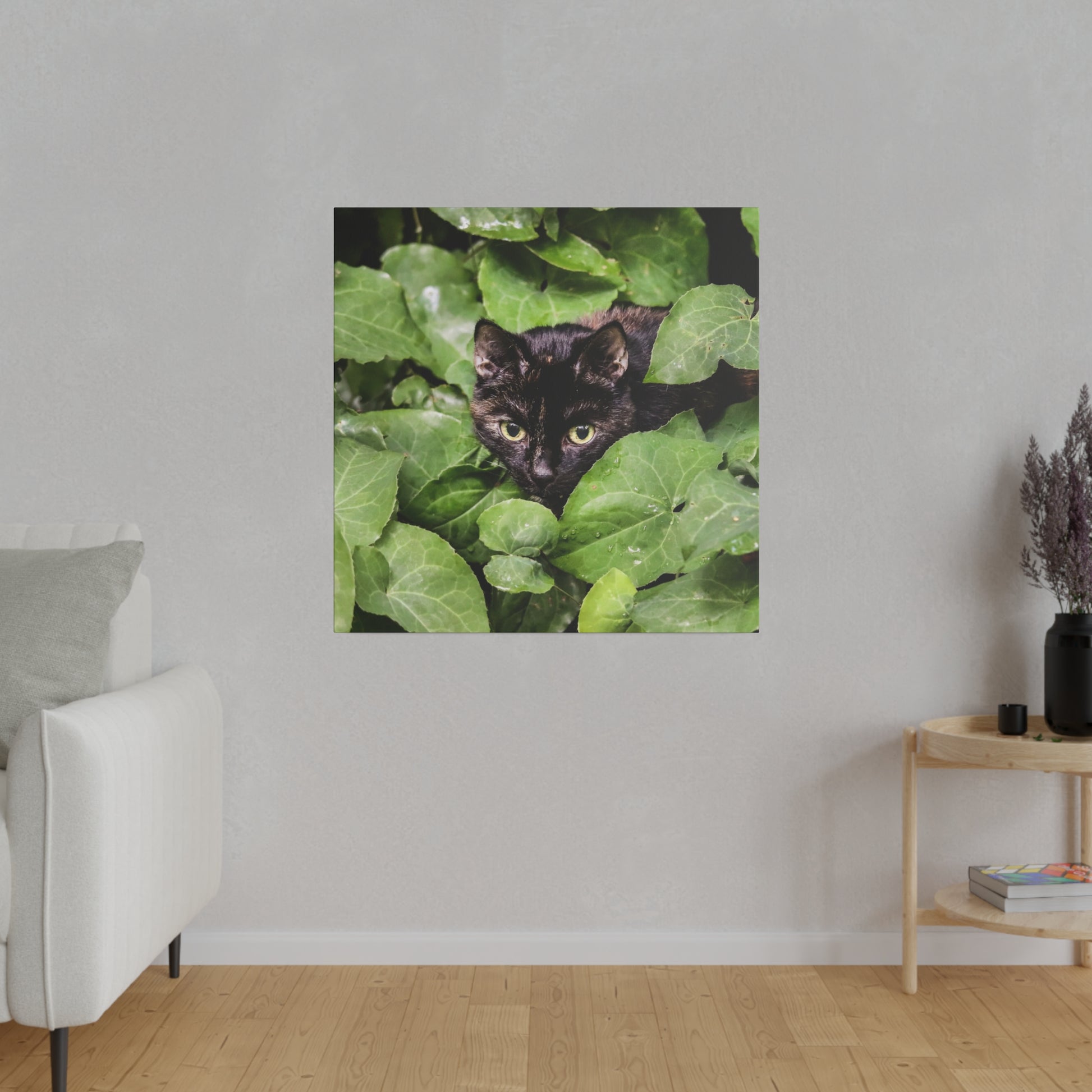 Black cat peeks through dense green ivy leaves in a square wall art photograph.