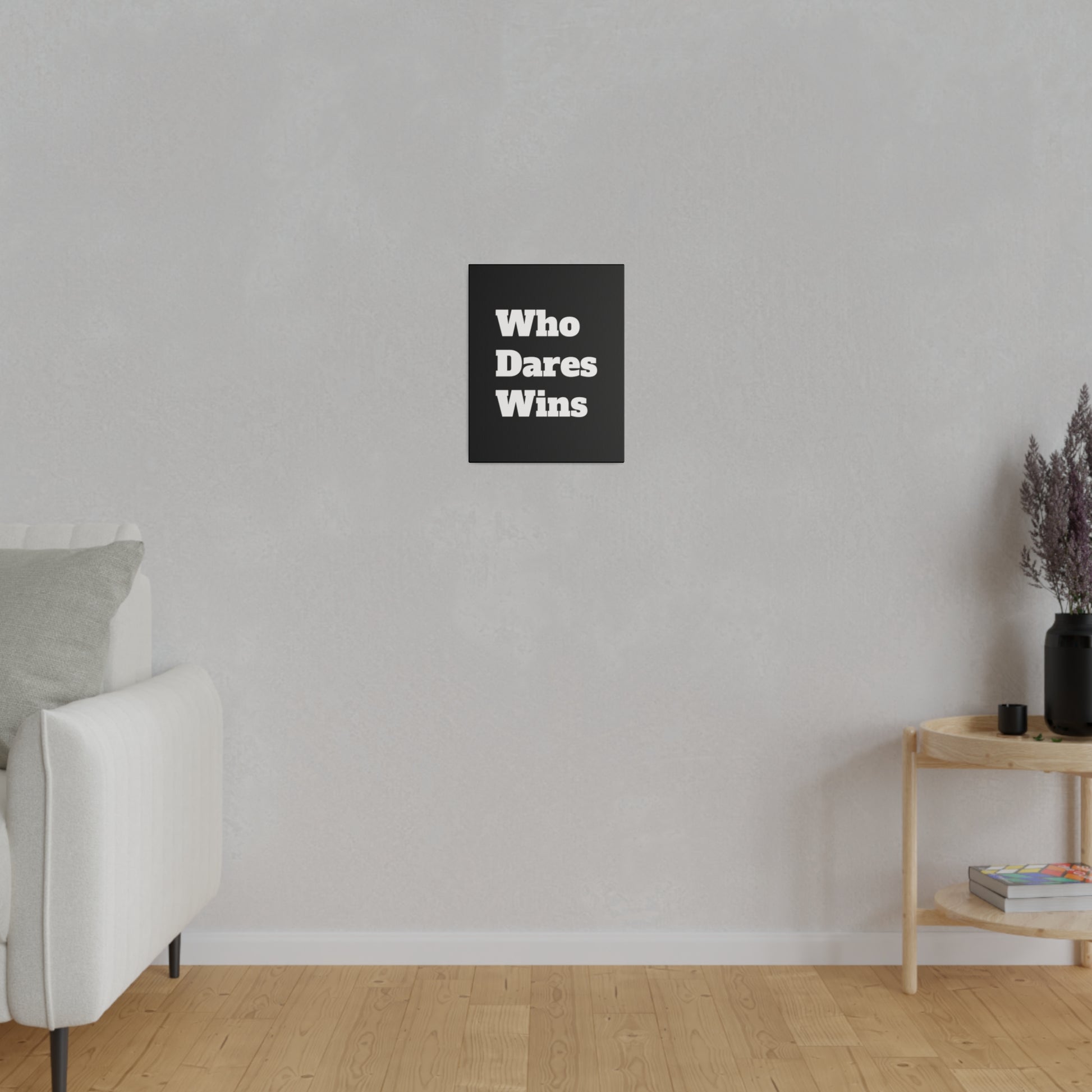 Light gray living room wall with a small black poster reading "Who Dares Wins" centered above a white sofa and wooden side table.