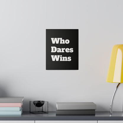Black poster with bold white “Who Dares Wins” text hangs on a light gray wall above a desk with stacked books and a yellow lamp.