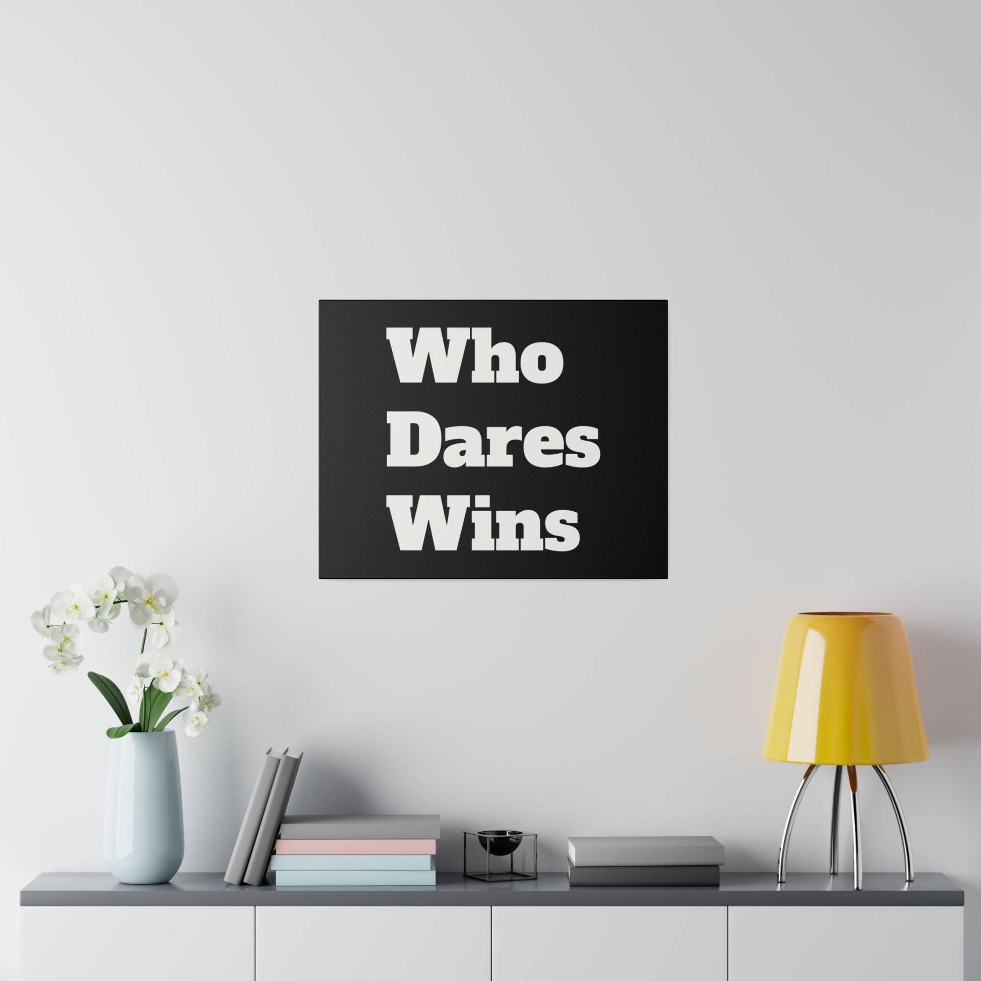 Black square wall art with white text "Who Dares Wins" above a shelf holding a vase of white orchids, stacked books, and a yellow lamp.