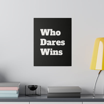 Black canvas with bold white text "Who Dares Wins" mounted on a light gray wall above a shelf with books and a yellow desk lamp.