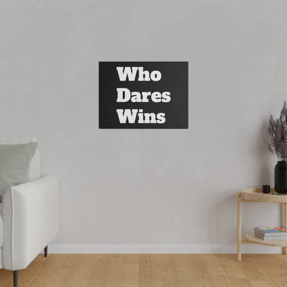Black wall art with white "Who Dares Wins" lettering hangs on a light gray wall above a wooden floor.