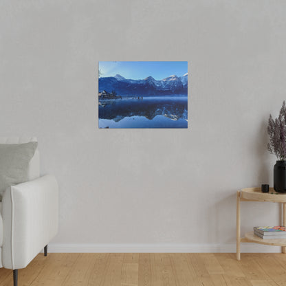 Blue photograph of a snow-capped mountain lake with reflections, mounted on a light gray wall.